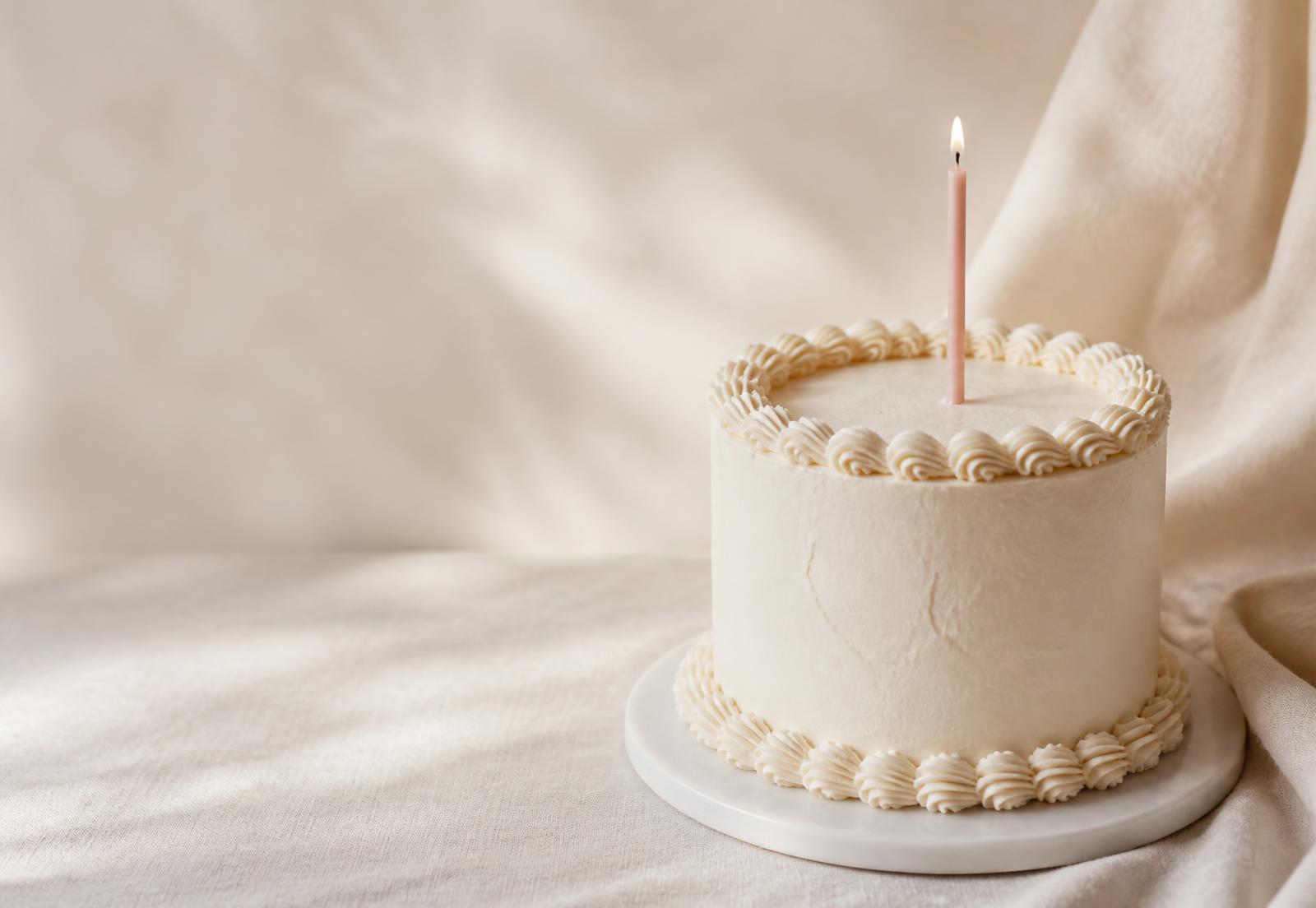 Cream frosted celebration cake with a single lit candle